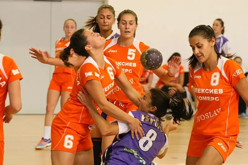 Handbollsspelare i orange tröja bryter sig fram mot två försvarare framför mållinjen