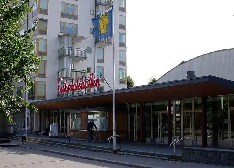 Entrén till en idrottshall i Stockholm med neonskylt, flaggstänger och cyklar utanför